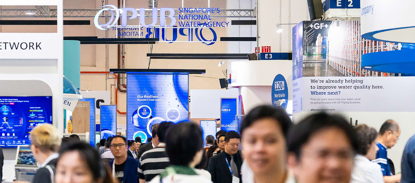 Crowd of people walking through an exhibition hall with signage for Singapore's national water agency and GF Piping Systems.