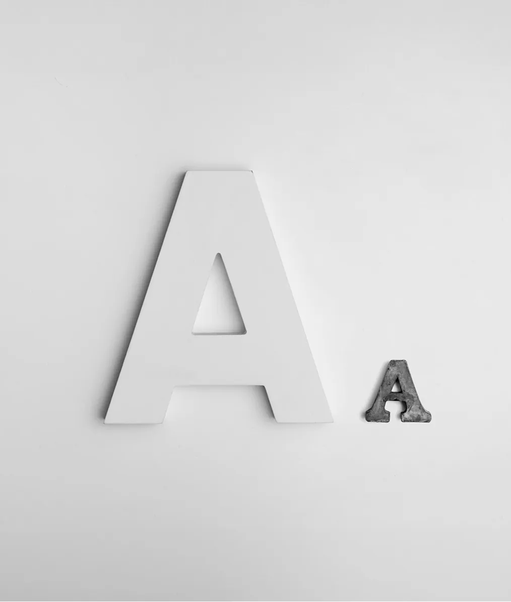 Two uppercase letter A's on a plain background, one large white and one small gray metal.
