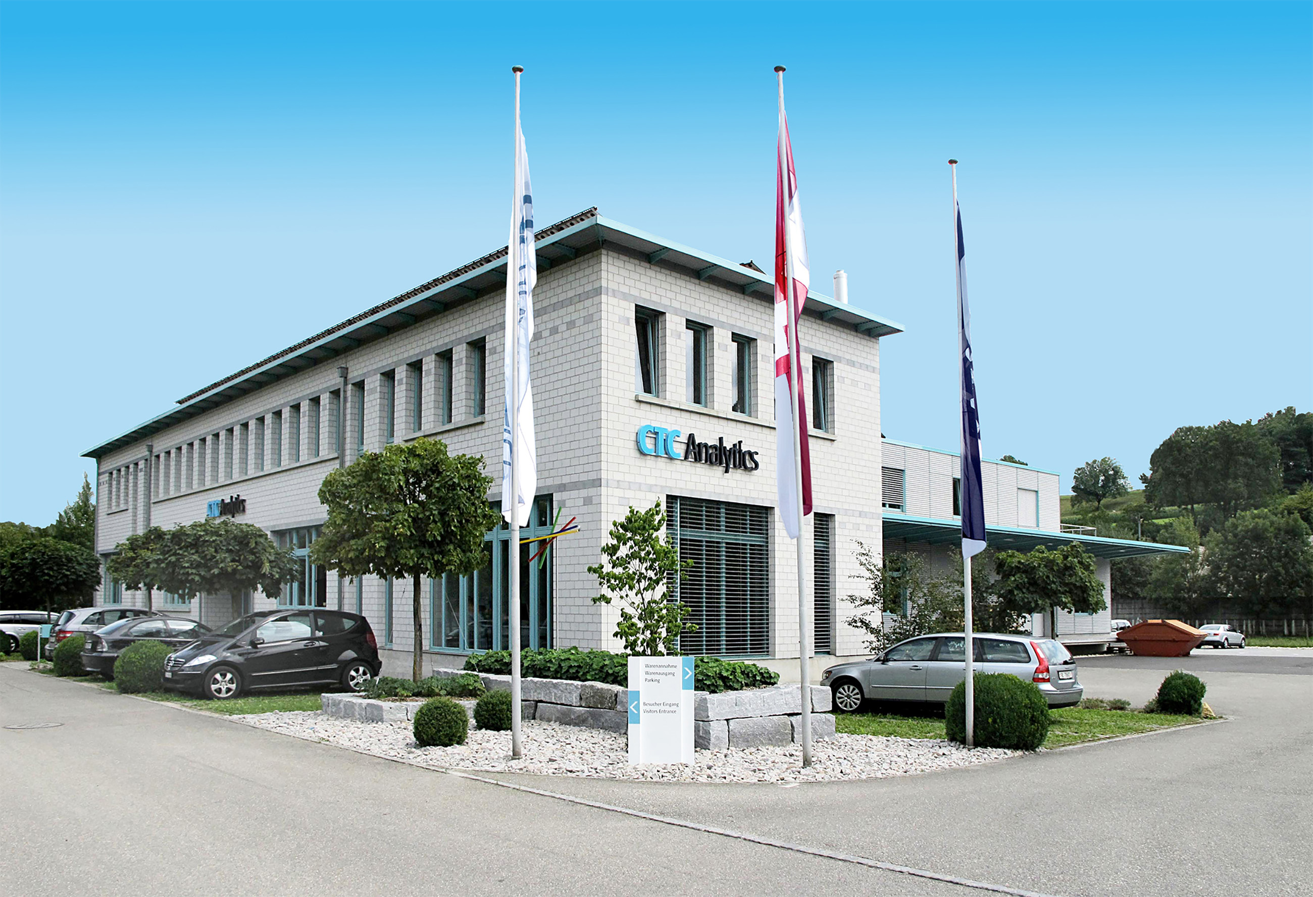 Modern CTC Analytics office building with flags, parked cars, and landscaped greenery under a clear blue sky.