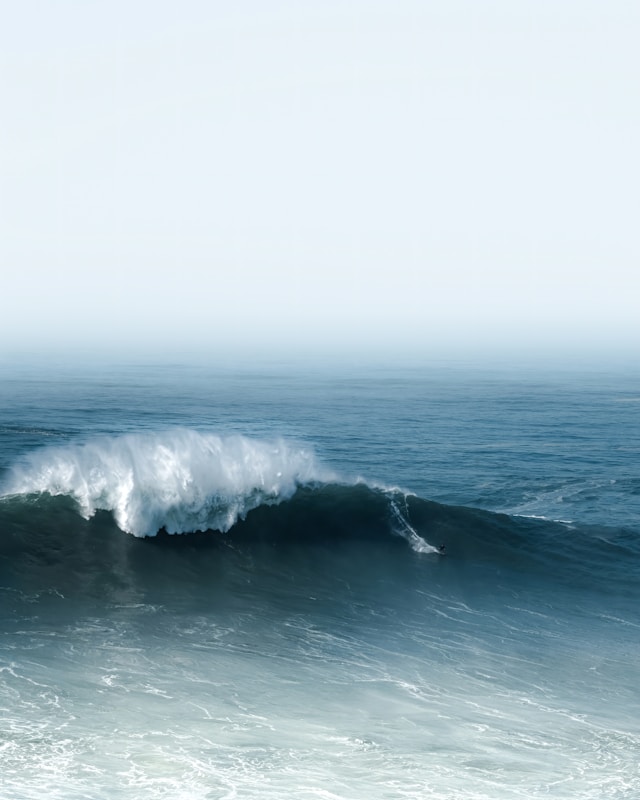 Large ocean wave breaking with a lone surfer riding the wave near the crest.
