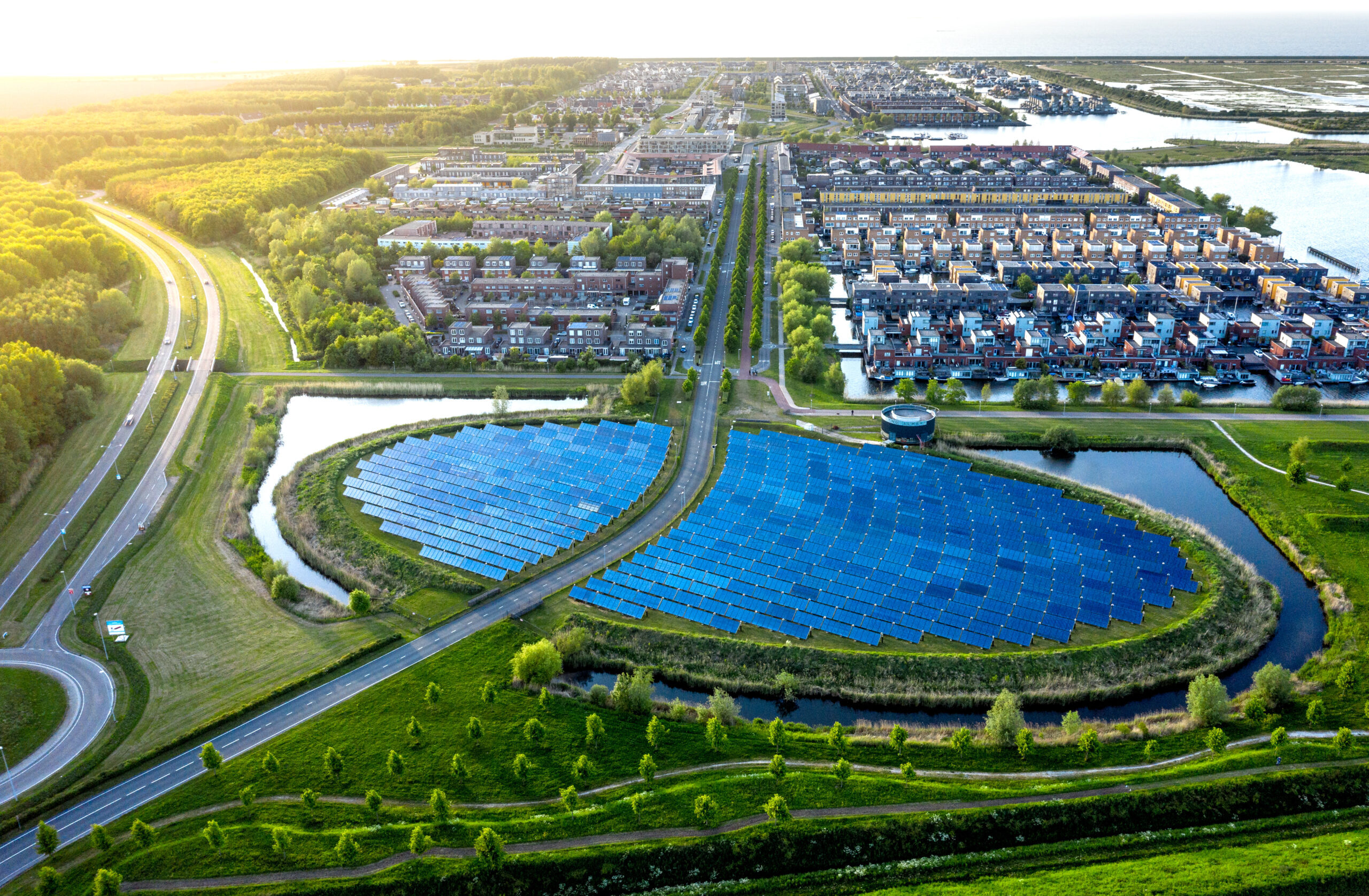 Aerial view of a residential neighborhood with two large curved solar panel arrays surrounded by water channels and greenery.