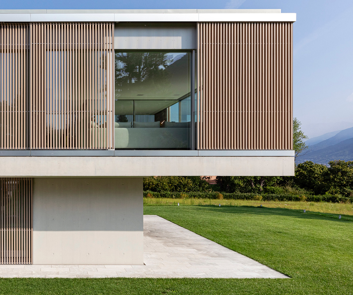 Modern two-story house with vertical wooden slats on the upper level and large glass windows overlooking a grassy lawn.