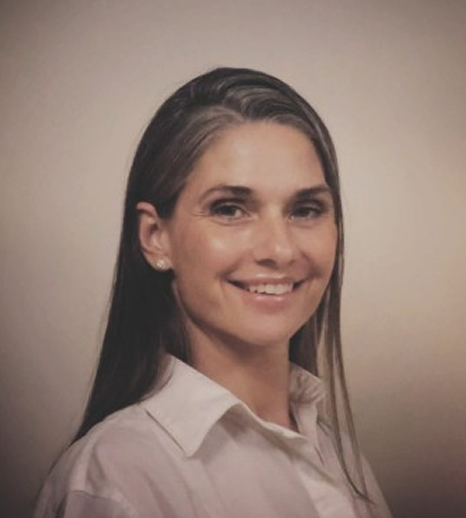 Smiling woman with long dark hair wearing a white collared shirt against a neutral background.