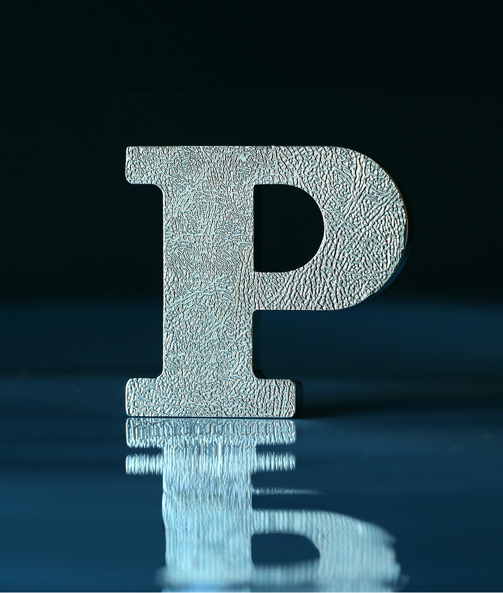 Textured metallic letter P standing on a reflective surface with its reflection visible below.