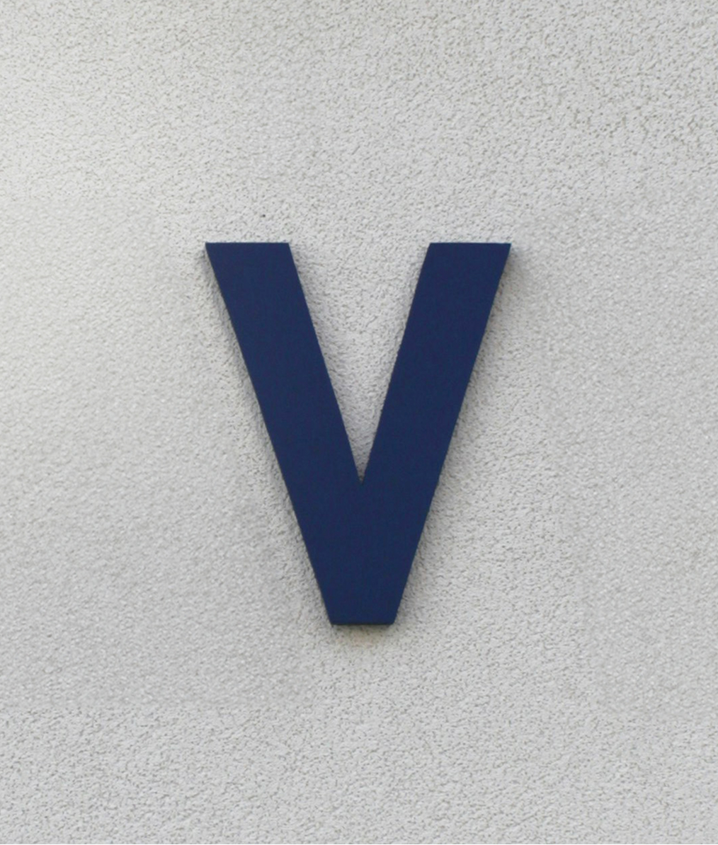 Dark blue letter V mounted on a light gray textured wall.