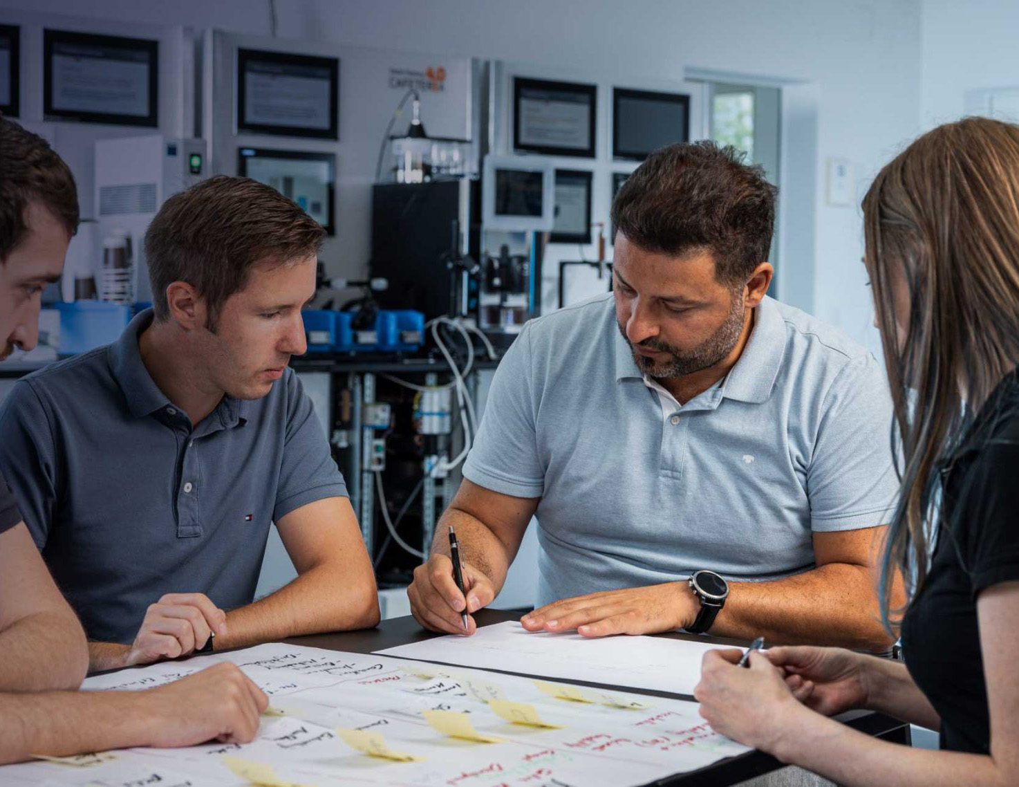 Four people sitting around a table, discussing and writing on large sheets of paper with notes.